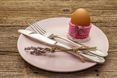 Easter table setting on vintage wooden boards background. Spring holiday card template. Cutlery, egg, lavender, bunny, knitted stand