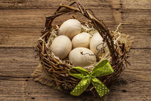 Easter wicker basket. Zero waste, DIY concept. Wooden eggs, shavings, satin bow. Old boards background, close up