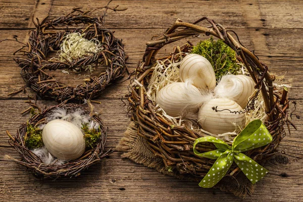 Easter wicker basket, birds nest, wreath. Zero waste, DIY concept. Wooden eggs, shavings, satin bow. Old boards background