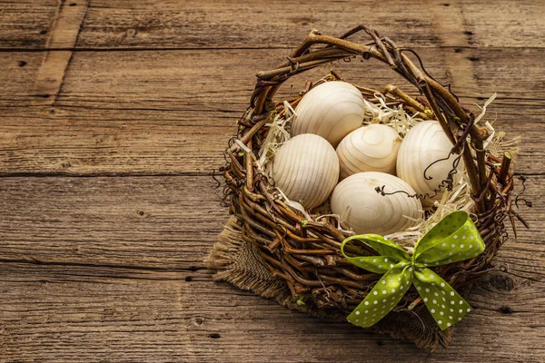 Easter wicker basket. Zero waste, DIY concept. Wooden eggs, shavings, satin bow. Old boards background, copy space