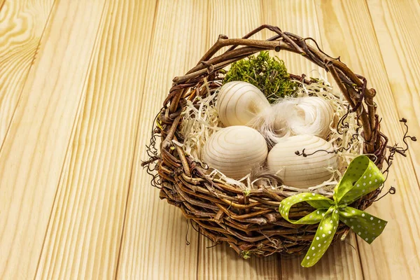 Easter wicker basket. Zero waste, DIY concept. Wooden eggs, shavings, satin bow. Boards background, copy space