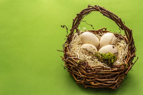 Easter wicker basket. Zero waste, DIY concept. Wooden eggs, shavings, moss. Green bright background, copy space