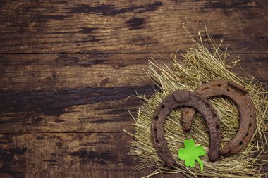 Saman üzerinde iki eski metal at nalı, yonca yaprağı. İyi şanslar sembolü, Aziz Patrick Günü konsepti. Antika ahşap arka plan, at aksesuarları.
