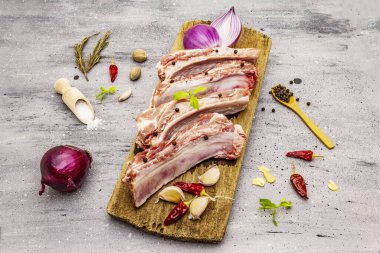 Gri taştan arka planda çiğ domuz pirzolası. Yuvarlak ahşap kesme tahtası, sebzeler, baharatlar ve yeşiller.