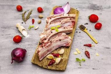 Gri taştan arka planda çiğ domuz pirzolası. Yuvarlak ahşap kesme tahtası, sebzeler, baharatlar ve yeşiller.