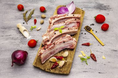 Gri taştan arka planda çiğ domuz pirzolası. Yuvarlak ahşap kesme tahtası, sebzeler, baharatlar ve yeşiller.