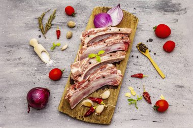 Gri taştan arka planda çiğ domuz pirzolası. Yuvarlak ahşap kesme tahtası, sebzeler, baharatlar ve yeşiller.