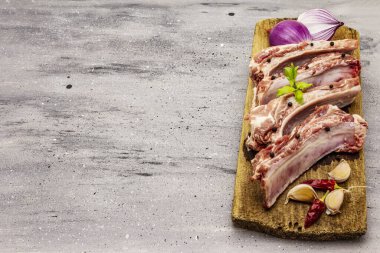 Gri taştan arka planda çiğ domuz pirzolası. Yuvarlak ahşap kesme tahtası, sebzeler, baharatlar ve yeşiller, kopyalama alanı