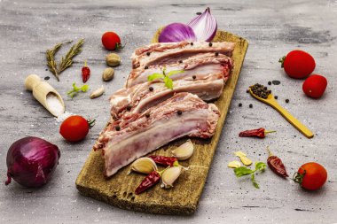 Gri taştan arka planda çiğ domuz pirzolası. Yuvarlak ahşap kesme tahtası, sebzeler, baharatlar ve yeşiller.