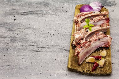 Gri taştan arka planda çiğ domuz pirzolası. Yuvarlak ahşap kesme tahtası, sebzeler, baharatlar ve yeşiller, kopyalama alanı, üst görünüm