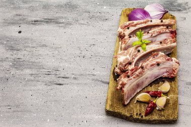 Gri taştan arka planda çiğ domuz pirzolası. Yuvarlak ahşap kesme tahtası, sebzeler, baharatlar ve yeşiller, kopyalama alanı