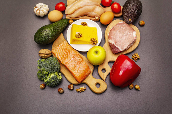 Trendy ketogenic diet products set. Paleo, pegan low carbs nutrition. Meat, fish, cheese, fruits and vegetables. Black stone concrete background