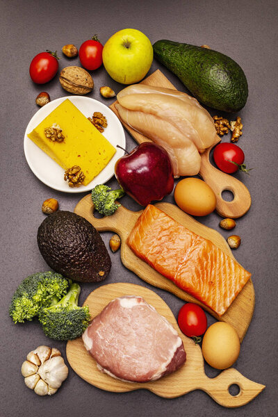 Trendy ketogenic diet products set. Paleo, pegan low carbs nutrition. Meat, fish, cheese, fruits and vegetables. Black stone concrete background