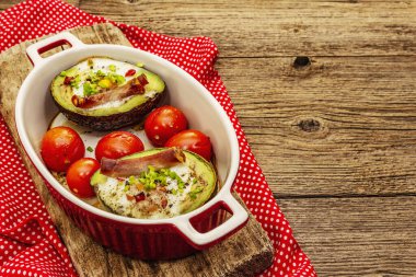 Güneşli sabah kahvaltısı. Avokado yarısı pişmiş yumurta, pastırma, domates, baharatlar. Sağlıklı yiyecekler, ketojenik diyet konsepti. Eski tahta arka plan