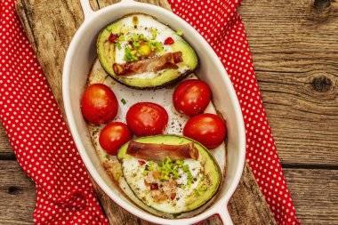 Güneşli sabah kahvaltısı. Avokado yarısı pişmiş yumurta, pastırma, domates, baharatlar. Sağlıklı yiyecekler, ketojenik diyet konsepti. Eski tahta arka plan