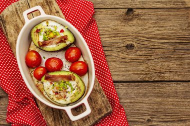 Güneşli sabah kahvaltısı. Avokado yarısı pişmiş yumurta, pastırma, domates, baharatlar. Sağlıklı yiyecekler, ketojenik diyet konsepti. Eski tahta arka plan