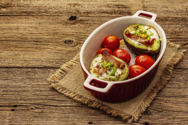 Güneşli sabah kahvaltısı. Avokado yarısı pişmiş yumurta, pastırma, domates, baharatlar. Sağlıklı yiyecekler, ketojenik diyet konsepti. Eski tahta arka plan