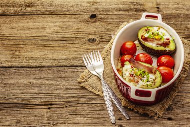 Güneşli sabah kahvaltısı. Avokado yarısı pişmiş yumurta, pastırma, domates, baharatlar. Sağlıklı yiyecekler, ketojenik diyet konsepti. Eski tahta arka plan