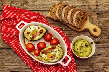 Güneşli sabah kahvaltısı. Avokado yarısı pişmiş yumurta, pastırma, domates, baharatlar. Sağlıklı yiyecekler, ketojenik diyet konsepti. Eski tahta arka plan