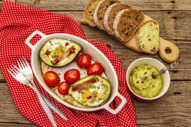 Güneşli sabah kahvaltısı. Avokado yarısı pişmiş yumurta, pastırma, domates, baharatlar. Sağlıklı yiyecekler, ketojenik diyet konsepti. Eski tahta arka plan