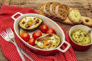 Güneşli sabah kahvaltısı. Avokado yarısı pişmiş yumurta, pastırma, domates, baharatlar. Sağlıklı yiyecekler, ketojenik diyet konsepti. Eski tahta arka plan