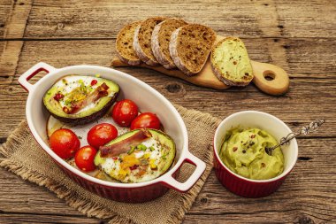 Güneşli sabah kahvaltısı. Avokado yarısı pişmiş yumurta, pastırma, domates, baharatlar. Sağlıklı yiyecekler, ketojenik diyet konsepti. Eski tahta arka plan