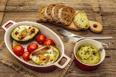 Güneşli sabah kahvaltısı. Avokado yarısı pişmiş yumurta, pastırma, domates, baharatlar. Sağlıklı yiyecekler, ketojenik diyet konsepti. Eski tahta arka plan