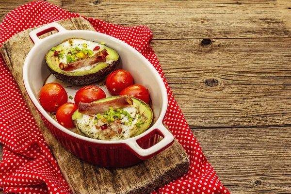 Güneşli sabah kahvaltısı. Avokado yarısı pişmiş yumurta, pastırma, domates, baharatlar. Sağlıklı yiyecekler, ketojenik diyet konsepti. Eski tahta arka plan