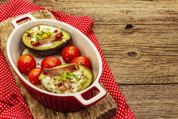 Güneşli sabah kahvaltısı. Avokado yarısı pişmiş yumurta, pastırma, domates, baharatlar. Sağlıklı yiyecekler, ketojenik diyet konsepti. Eski tahta arka plan