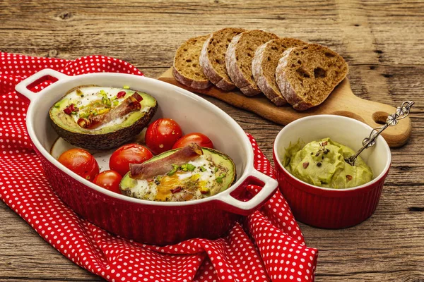 Güneşli sabah kahvaltısı. Avokado yarısı pişmiş yumurta, pastırma, domates, baharatlar. Sağlıklı yiyecekler, ketojenik diyet konsepti. Eski tahta arka plan