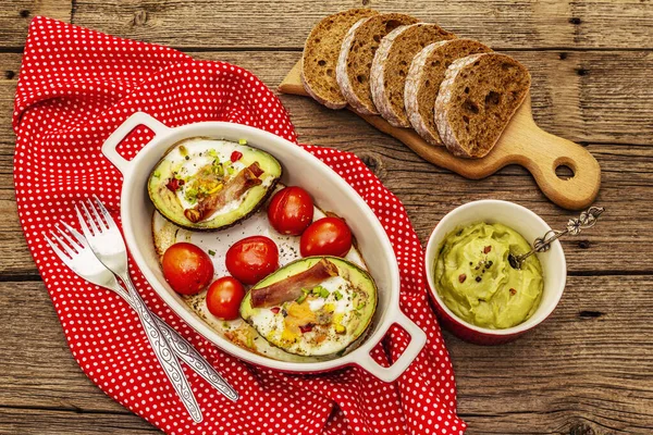 Güneşli sabah kahvaltısı. Avokado yarısı pişmiş yumurta, pastırma, domates, baharatlar. Sağlıklı yiyecekler, ketojenik diyet konsepti. Eski tahta arka plan