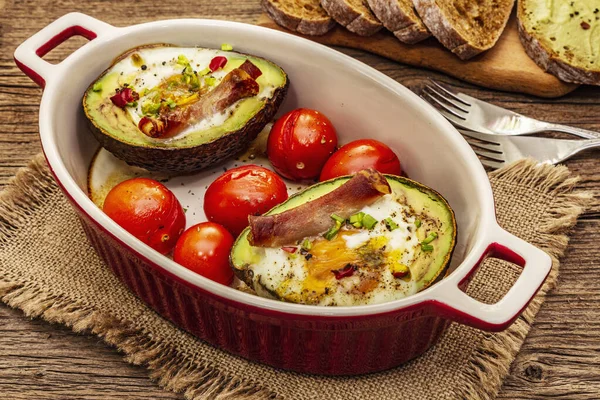 Güneşli sabah kahvaltısı. Avokado yarısı pişmiş yumurta, pastırma, domates, baharatlar. Sağlıklı yiyecekler, ketojenik diyet konsepti. Eski tahta arka plan