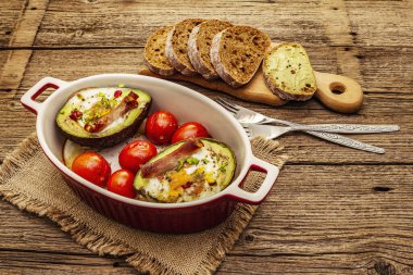 Güneşli sabah kahvaltısı. Avokado yarısı pişmiş yumurta, pastırma, domates, baharatlar. Sağlıklı yiyecekler, ketojenik diyet konsepti. Eski tahta arka plan