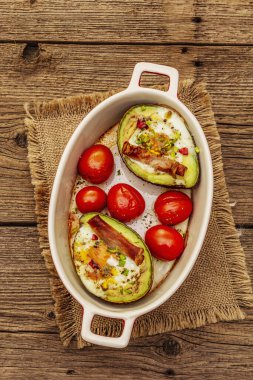 Güneşli sabah kahvaltısı. Avokado yarısı pişmiş yumurta, pastırma, domates, baharatlar. Sağlıklı yiyecekler, ketojenik diyet konsepti. Eski tahta arka plan