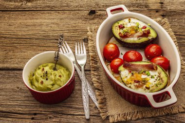 Güneşli sabah kahvaltısı. Avokado yarısı pişmiş yumurta, pastırma, domates, baharatlar. Sağlıklı yiyecekler, ketojenik diyet konsepti. Eski tahta arka plan