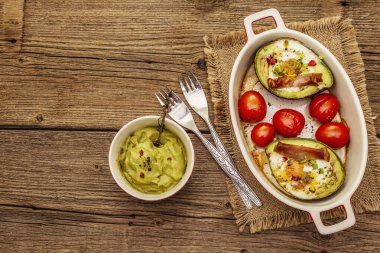 Güneşli sabah kahvaltısı. Avokado yarısı pişmiş yumurta, pastırma, domates, baharatlar. Sağlıklı yiyecekler, ketojenik diyet konsepti. Eski tahta arka plan