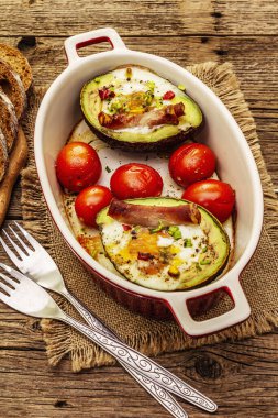 Güneşli sabah kahvaltısı. Avokado yarısı pişmiş yumurta, pastırma, domates, baharatlar. Sağlıklı yiyecekler, ketojenik diyet konsepti. Eski tahta arka plan