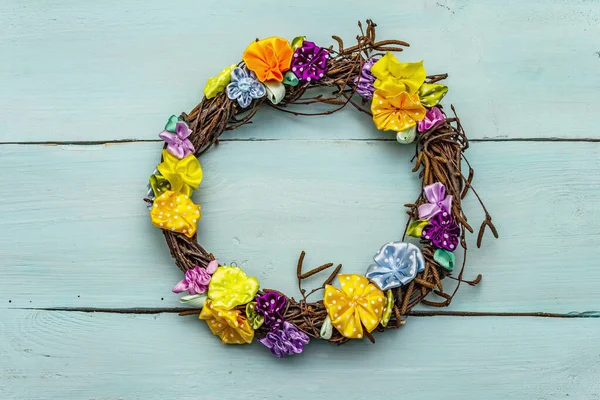 Spring composition of a wreath of birch branches and craft colorful flowers. Handmade from satin polka dot ribbons, stay at home concept. Turquoise wooden background