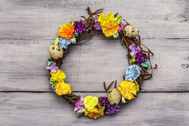 El yapımı Paskalya hasır çelengi, bıldırcın yumurtası ve el yapımı çiçeklerle. Ağaç dalları, benekli saten kurdele. Ev konseptinde kal. Bayramlık Paskalya Gri ahşap arka plan, üst manzara