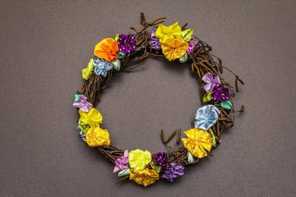 Spring composition of a wreath of birch branches and craft colorful flowers. Handmade from satin polka dot ribbons, stay at home concept. Black stone background, top view