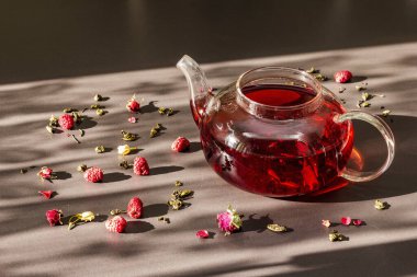 Güneşli sabah kahvaltısı. Kuru meyve, çiçek ve yapraklı çaydanlık içinde ahududu yeşili çay. Moda siyah taş arkaplan