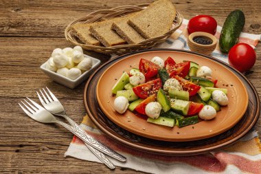 Domates, salatalık ve bebek mozzarellasından taze salata. Kabuklu ekmekle güneşli bir öğle yemeği. Eski tahta arka plan