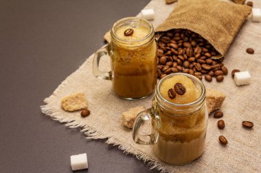 Duvarcı kavanozunda Dalgona kahvesi. Kore kremalı kahve içeceği. Siyah taş arka planda moda karantina içeceği, şeker ve kahve çekirdekleri