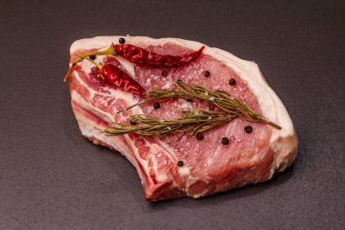 Moda siyah taş arka planda çiğ domuz eti. Baharatlar, deniz tuzu, biberiye, biber biberi, yakın çekim.