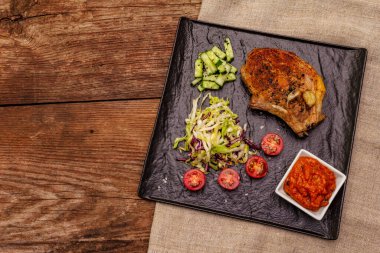 Izgara domuz bifteği. Cole yavaş salatası, domates sosu, taze sebzeler. Eski ahşap masa, üst manzara.