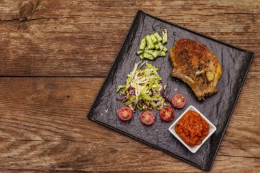 Izgara domuz bifteği. Cole yavaş salatası, domates sosu, taze sebzeler. Eski ahşap masa, üst manzara.