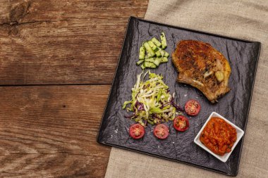 Izgara domuz bifteği. Cole yavaş salatası, domates sosu, taze sebzeler. Eski ahşap masa, üst manzara.