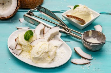 Laktozsuz hindistan cevizli dondurma. Özel kaşık, yarım meyve, gevrek. Vejetaryen tatlı konsepti. Moda turkuaz ahşap tahta arka plan