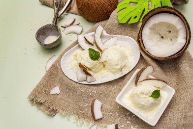 Laktozsuz hindistan cevizli dondurma. Özel kaşık, yarım meyve, gevrek. Vejetaryen tatlı konsepti. Açık yeşil arkaplan