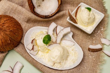 Laktozsuz hindistan cevizli dondurma. Özel kaşık, yarım meyve, gevrek. Vejetaryen tatlı konsepti. Açık yeşil arkaplan